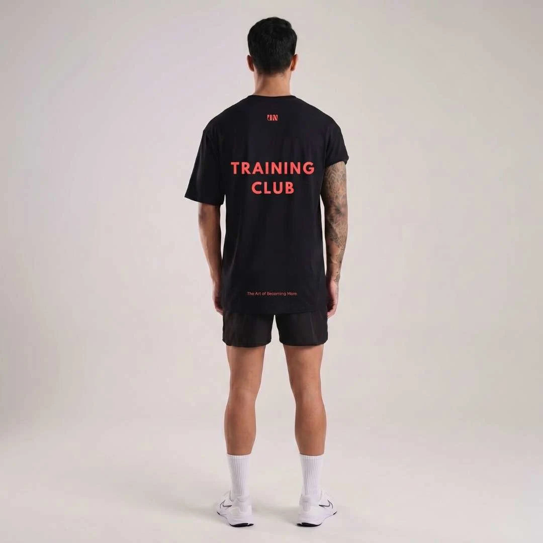 Person wearing a Unproven black oversize boxy fit t-shirt with 'TRAINING CLUB' text on the back against a plain background best for gyms, workouts running
