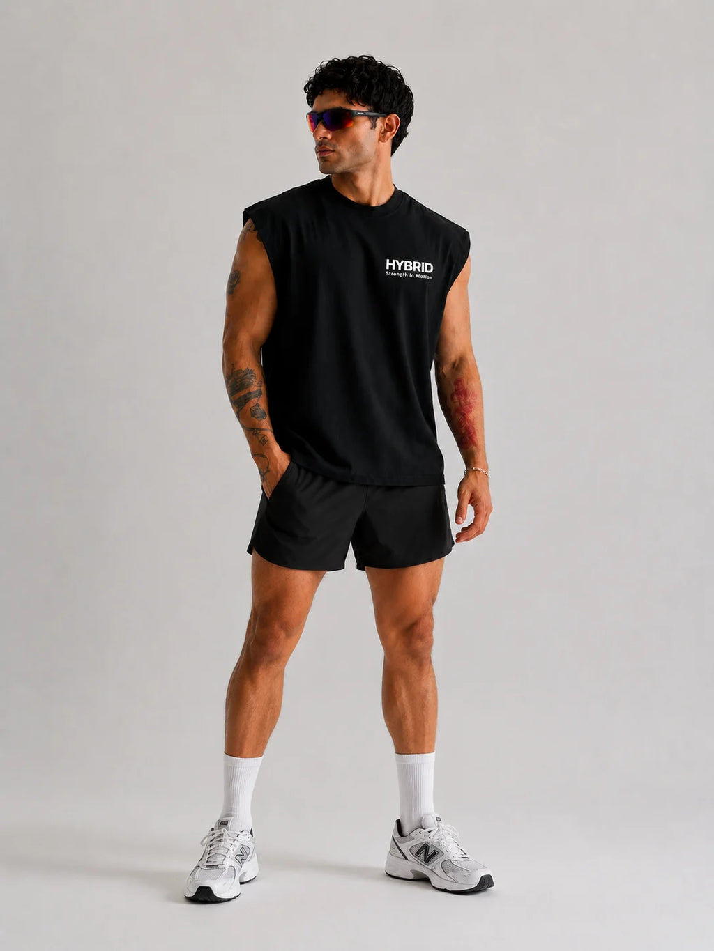 Man wearing a Best Unproven black sleeveless tank or boxy fit tank with 'Hybrid' logo on a gray background